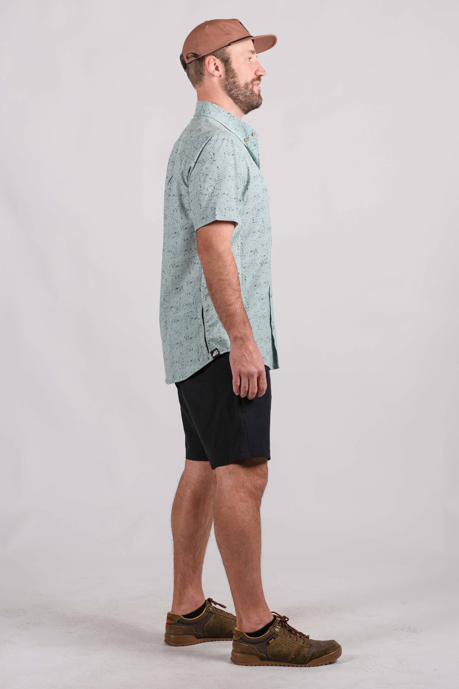 The Vista Stretch Button Down from Belong Designs features a modern, casual design in Summit Teal. This short-sleeve shirt includes a buttoned-down collar and is crafted from wrinkle-resistant fabric. It also comes with a small chest pocket adorned with a logo patch reading "Belong Designs.
