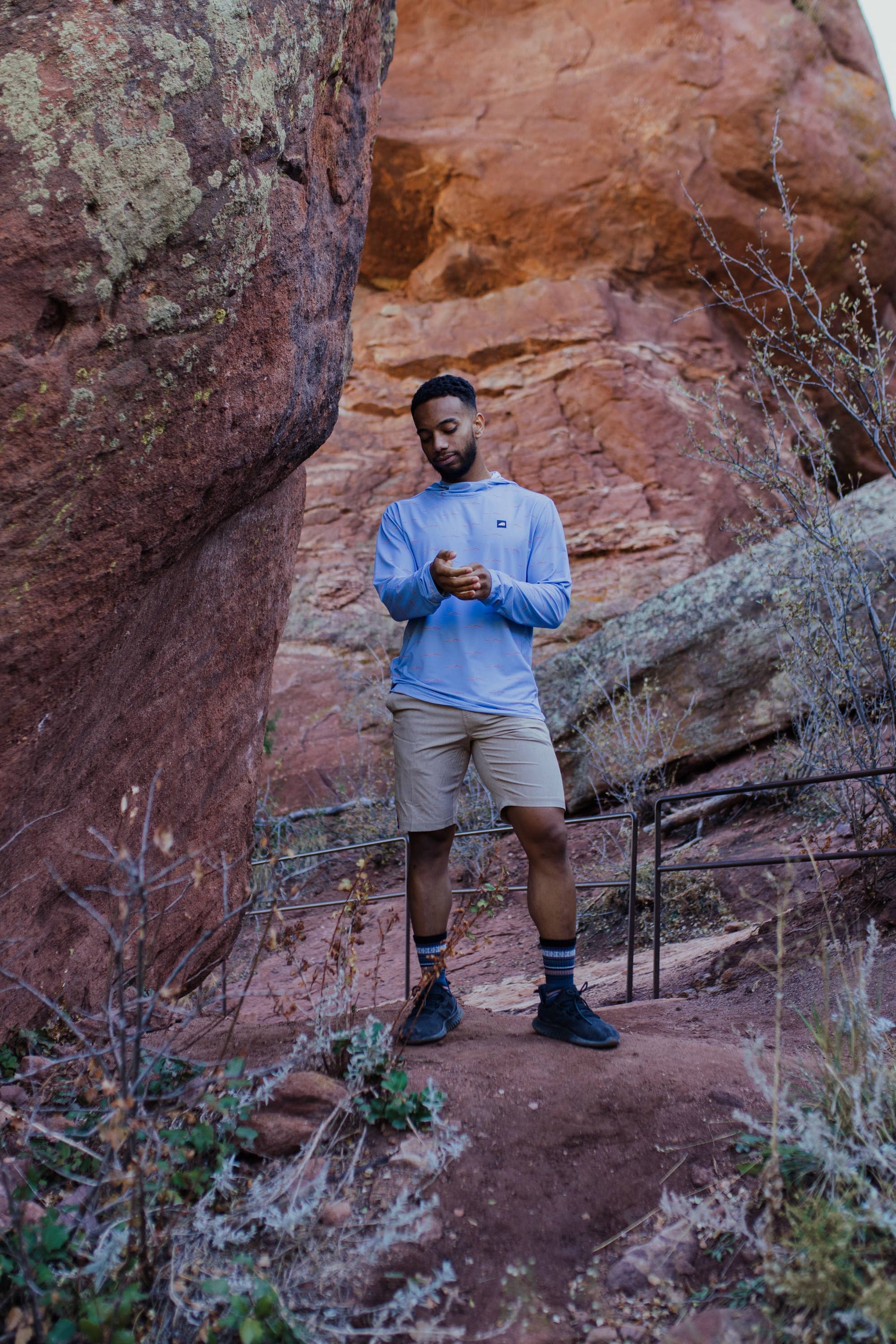 A man is wearing a Belong Designs Men's Sun Hoodie in Green Block, paired with black shorts. The hoodie features a small black logo on the left chest and offers UPF 50+ protection. He is standing against a plain, light-colored background, ready for outdoor activities. His head is not visible in the image.