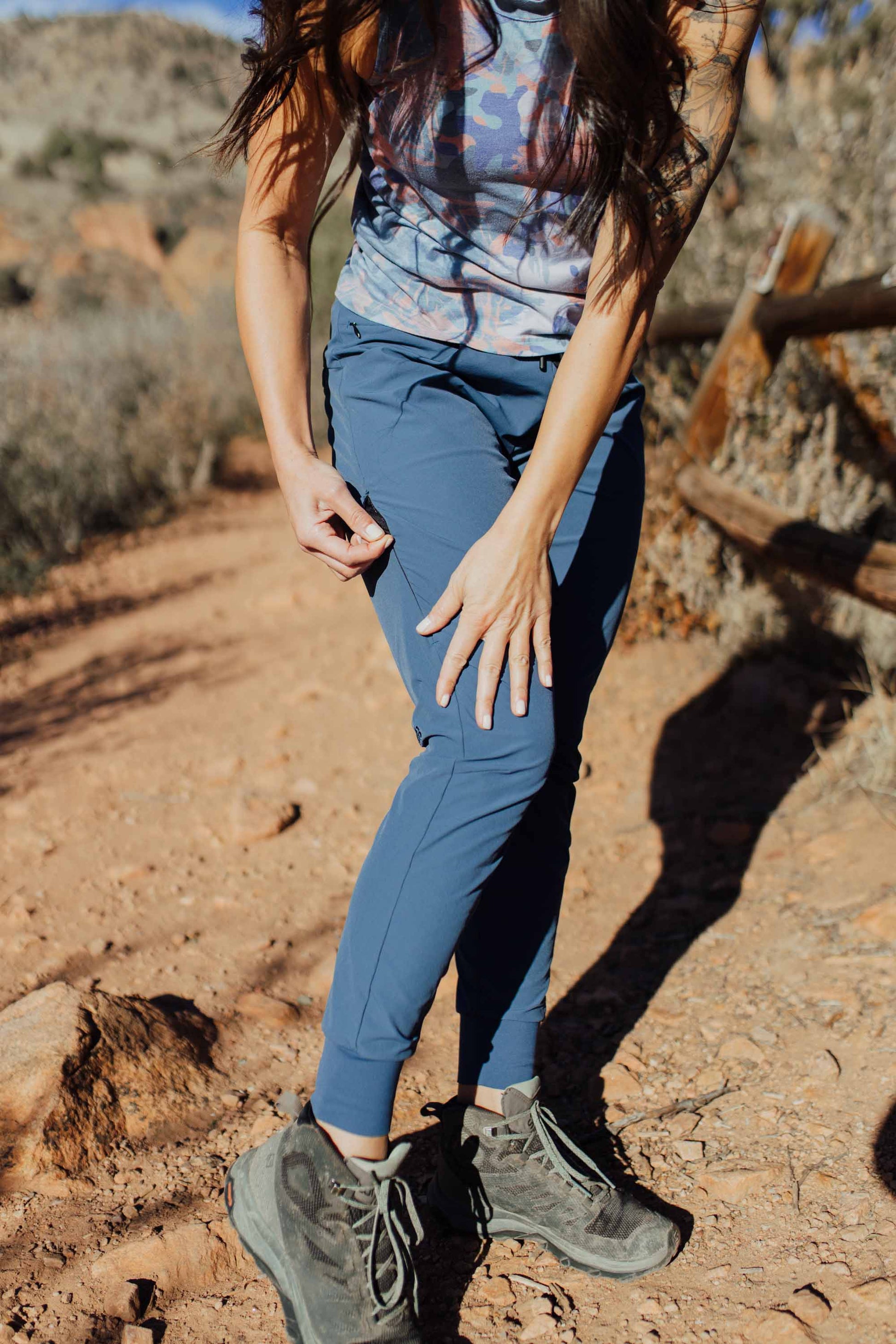 A person wearing Belong Designs' Rocky Mountain Joggers, crafted from durable and stretchy material, stands against a plain background. They are dressed in a dark green cropped top paired with matching athletic pants featuring a drawstring, complemented by brown hiking boots with teal laces. The image is cropped to show the midriff down.
