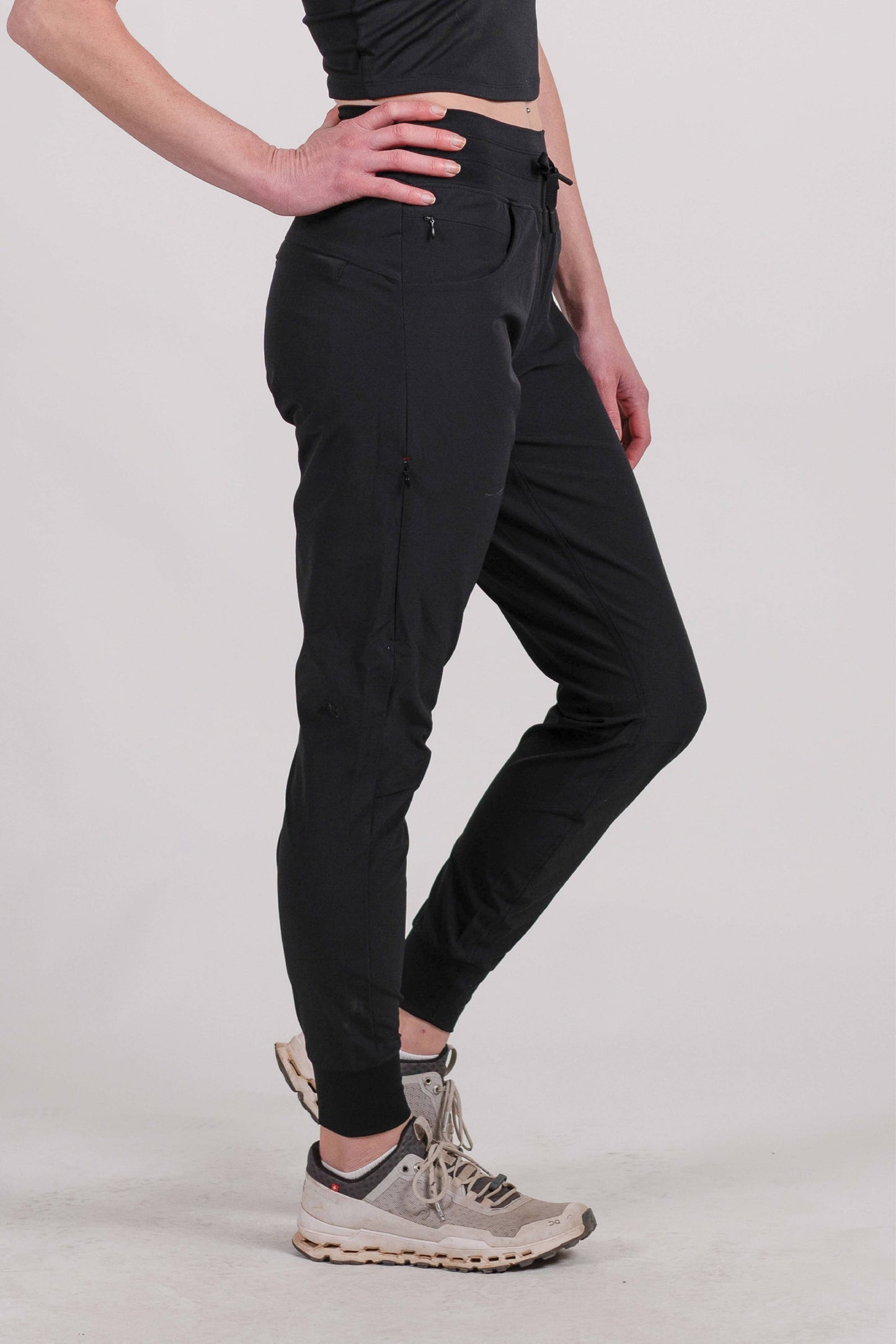 A person wearing Belong Designs' Rocky Mountain Joggers, crafted from durable and stretchy material, stands against a plain background. They are dressed in a dark green cropped top paired with matching athletic pants featuring a drawstring, complemented by brown hiking boots with teal laces. The image is cropped to show the midriff down.
