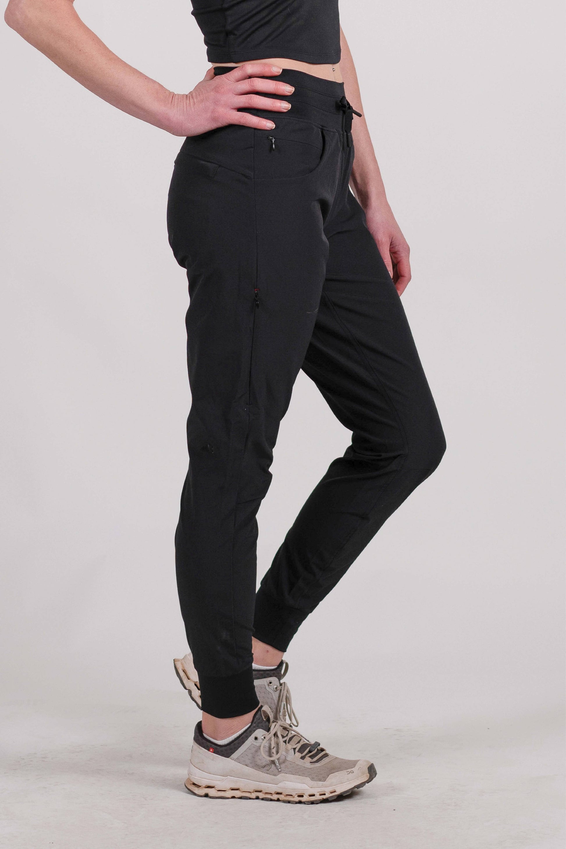 A person wearing Belong Designs' Rocky Mountain Joggers, crafted from durable and stretchy material, stands against a plain background. They are dressed in a dark green cropped top paired with matching athletic pants featuring a drawstring, complemented by brown hiking boots with teal laces. The image is cropped to show the midriff down.
