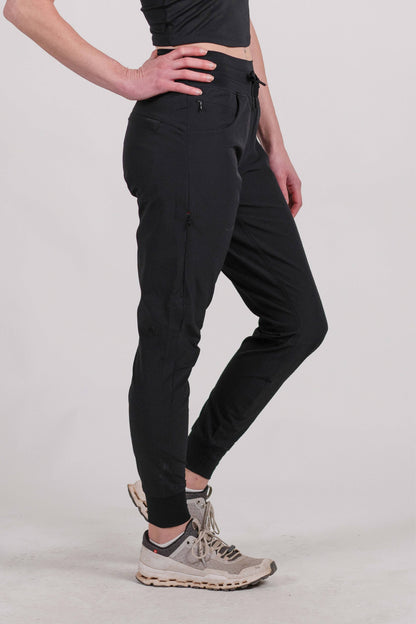 A person wearing Belong Designs' Rocky Mountain Joggers, crafted from durable and stretchy material, stands against a plain background. They are dressed in a dark green cropped top paired with matching athletic pants featuring a drawstring, complemented by brown hiking boots with teal laces. The image is cropped to show the midriff down.
