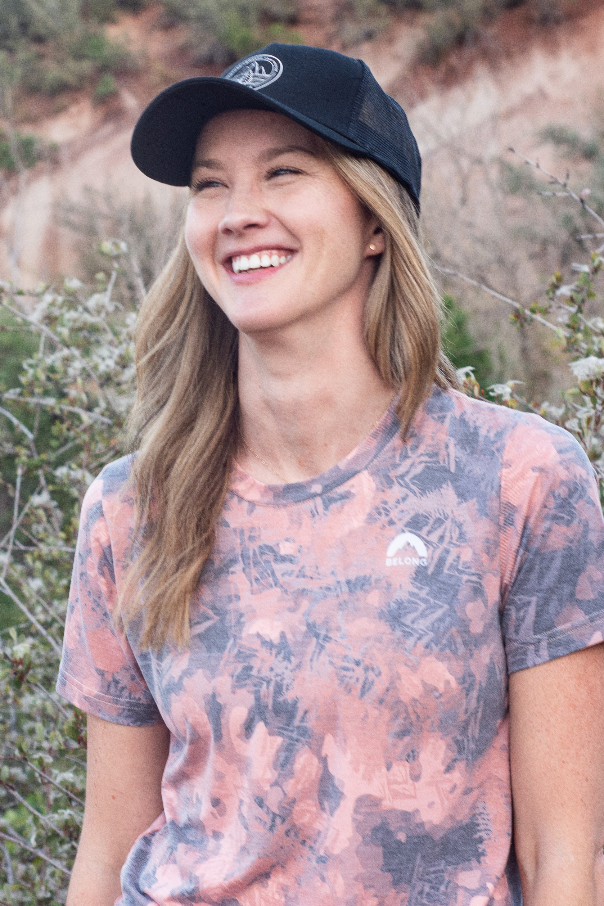 The Every Trail Trucker Hat by Belong Designs is a Black Mountain Brush trucker hat with a curved brim. The front panel showcases a vibrant wavy line design in shades of red, yellow, blue, and white with "BELONG" emblazoned prominently. The back and sides are made of breathable white mesh for added comfort.