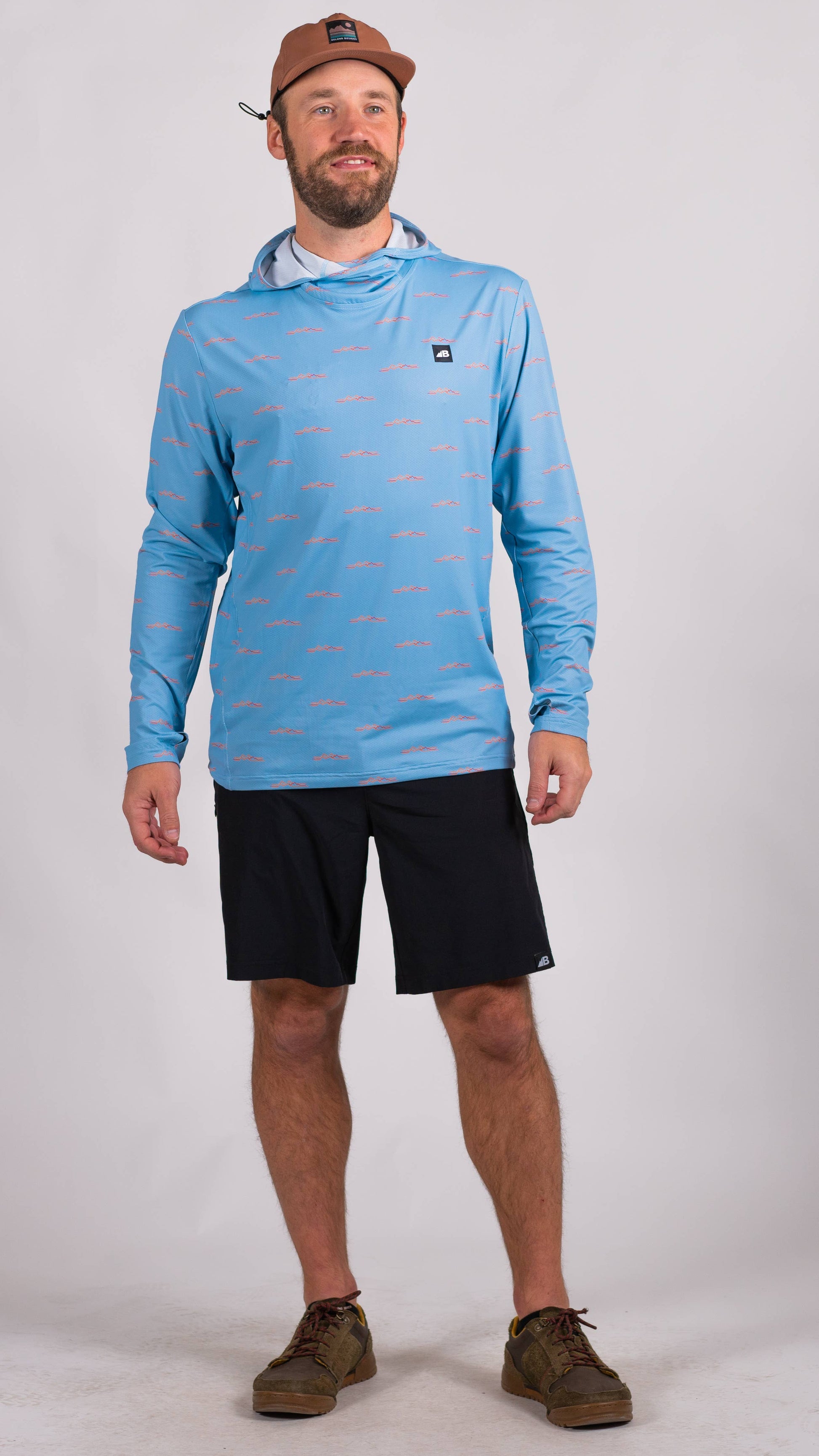 A man is wearing a Belong Designs Men's Sun Hoodie in Green Block, paired with black shorts. The hoodie features a small black logo on the left chest and offers UPF 50+ protection. He is standing against a plain, light-colored background, ready for outdoor activities. His head is not visible in the image.