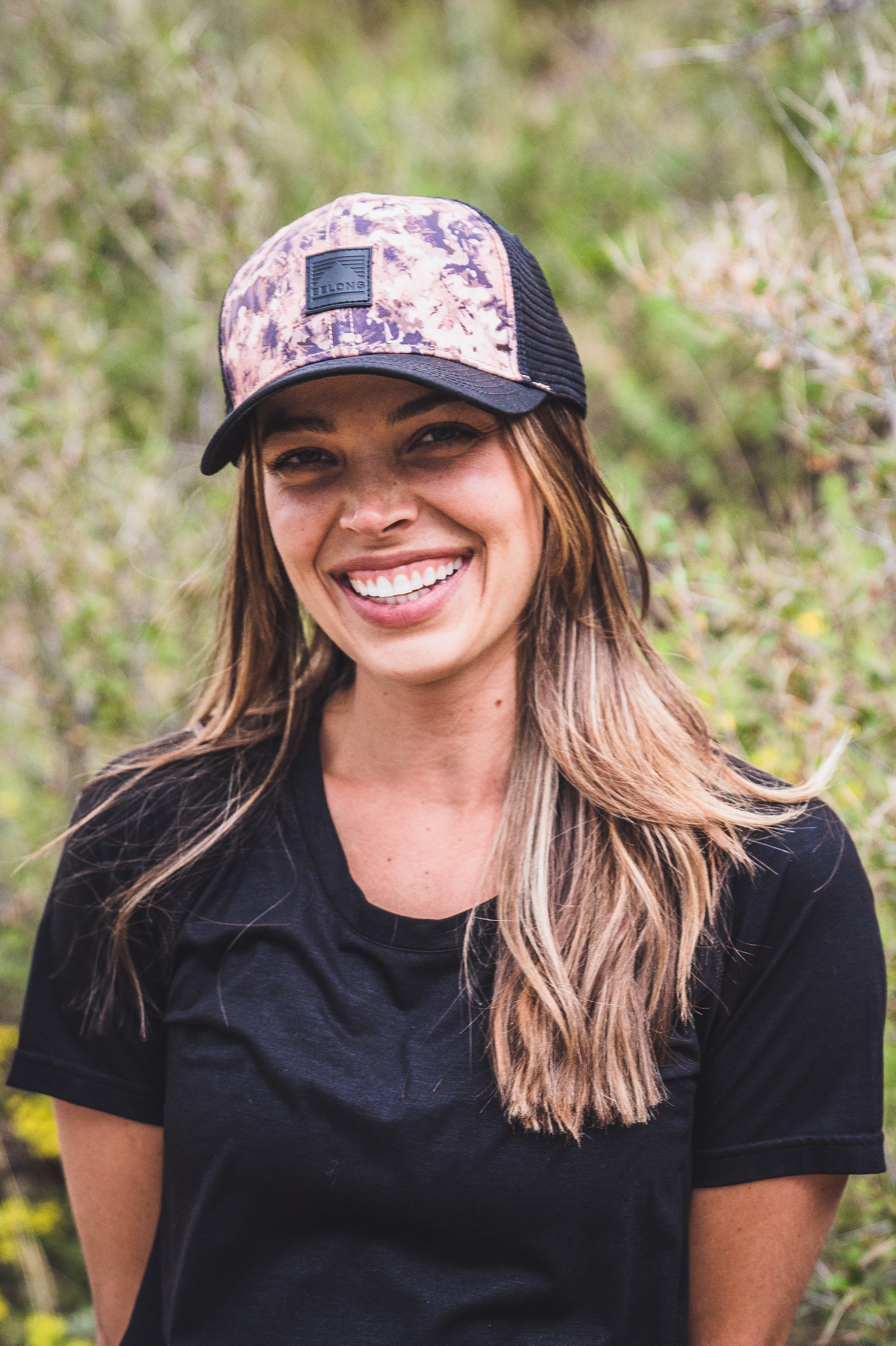 The Every Trail Trucker Hat by Belong Designs is a Black Mountain Brush trucker hat with a curved brim. The front panel showcases a vibrant wavy line design in shades of red, yellow, blue, and white with "BELONG" emblazoned prominently. The back and sides are made of breathable white mesh for added comfort.