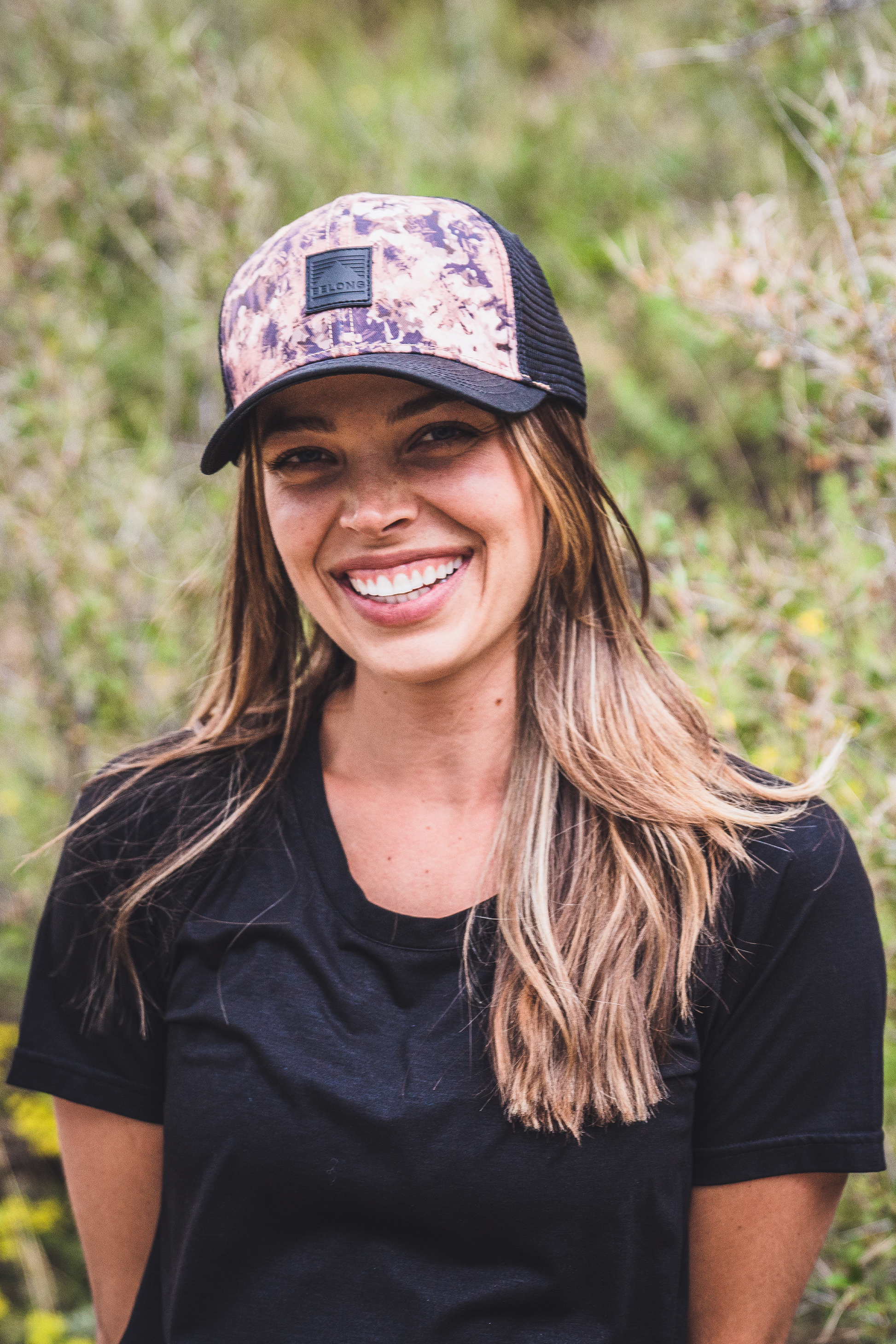The Every Trail Trucker Hat by Belong Designs is a Black Mountain Brush trucker hat with a curved brim. The front panel showcases a vibrant wavy line design in shades of red, yellow, blue, and white with "BELONG" emblazoned prominently. The back and sides are made of breathable white mesh for added comfort.