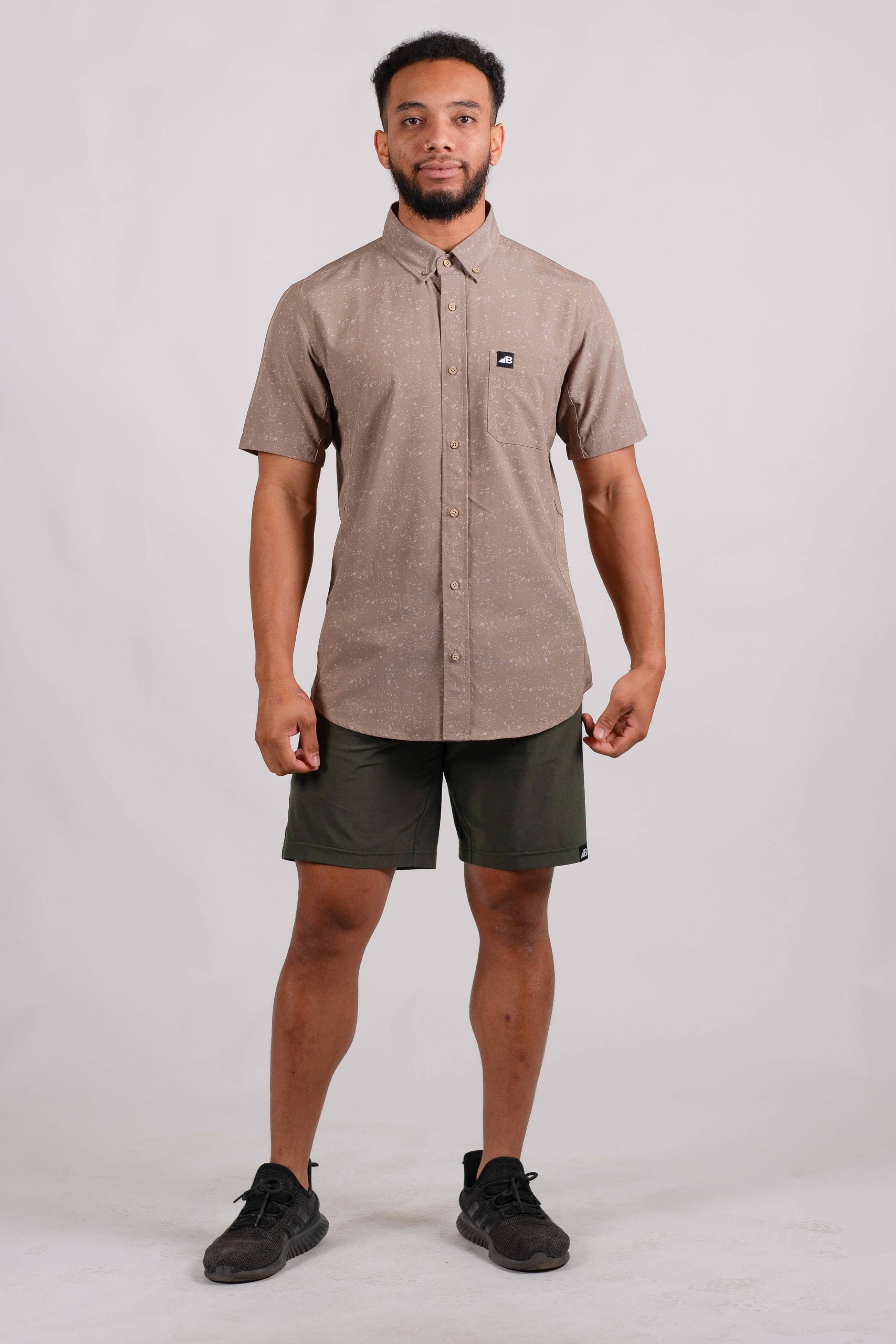 The Vista Stretch Button Down from Belong Designs features a modern, casual design in Summit Teal. This short-sleeve shirt includes a buttoned-down collar and is crafted from wrinkle-resistant fabric. It also comes with a small chest pocket adorned with a logo patch reading "Belong Designs.
