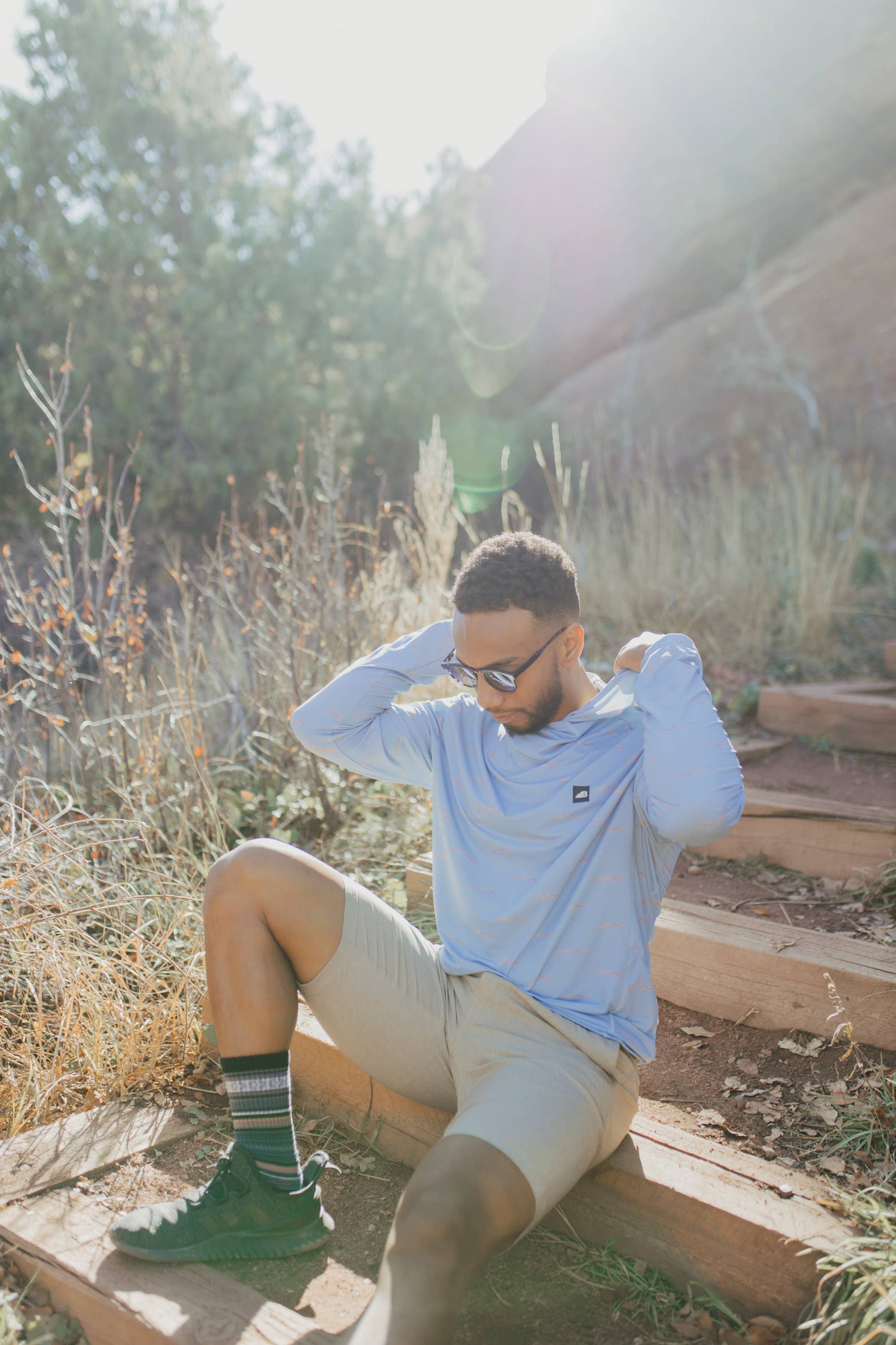 A man is wearing a Belong Designs Men's Sun Hoodie in Green Block, paired with black shorts. The hoodie features a small black logo on the left chest and offers UPF 50+ protection. He is standing against a plain, light-colored background, ready for outdoor activities. His head is not visible in the image.