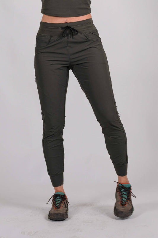 A person wearing Belong Designs' Rocky Mountain Joggers, crafted from durable and stretchy material, stands against a plain background. They are dressed in a dark green cropped top paired with matching athletic pants featuring a drawstring, complemented by brown hiking boots with teal laces. The image is cropped to show the midriff down.
