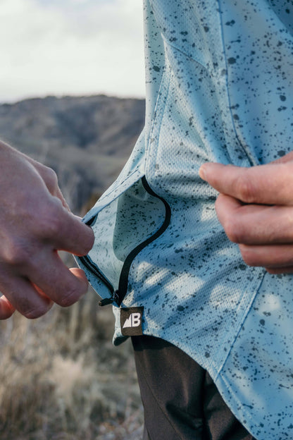 The Vista Stretch Button Down from Belong Designs features a modern, casual design in Summit Teal. This short-sleeve shirt includes a buttoned-down collar and is crafted from wrinkle-resistant fabric. It also comes with a small chest pocket adorned with a logo patch reading "Belong Designs.