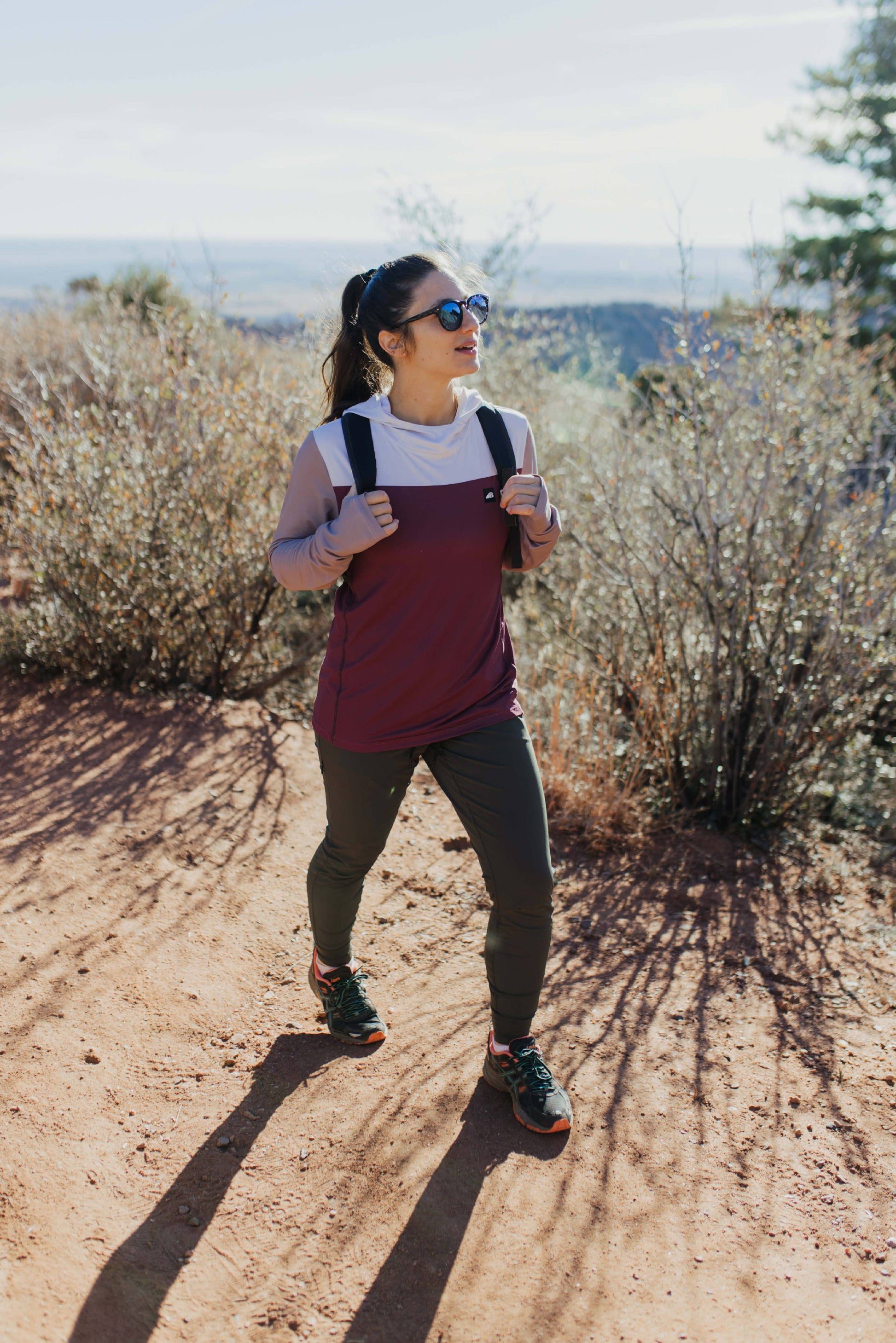 A person wearing Belong Designs' Rocky Mountain Joggers, crafted from durable and stretchy material, stands against a plain background. They are dressed in a dark green cropped top paired with matching athletic pants featuring a drawstring, complemented by brown hiking boots with teal laces. The image is cropped to show the midriff down.
