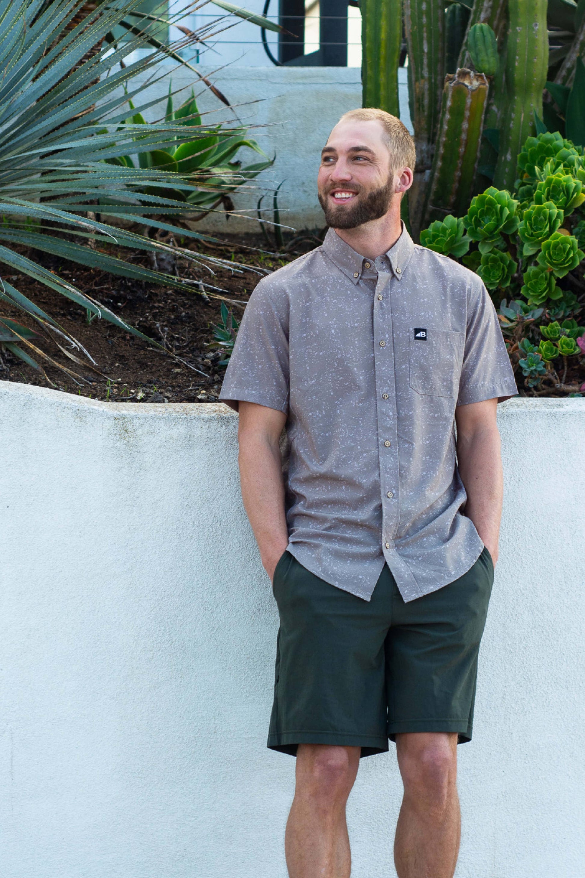 The Vista Stretch Button Down from Belong Designs features a modern, casual design in Summit Teal. This short-sleeve shirt includes a buttoned-down collar and is crafted from wrinkle-resistant fabric. It also comes with a small chest pocket adorned with a logo patch reading "Belong Designs.