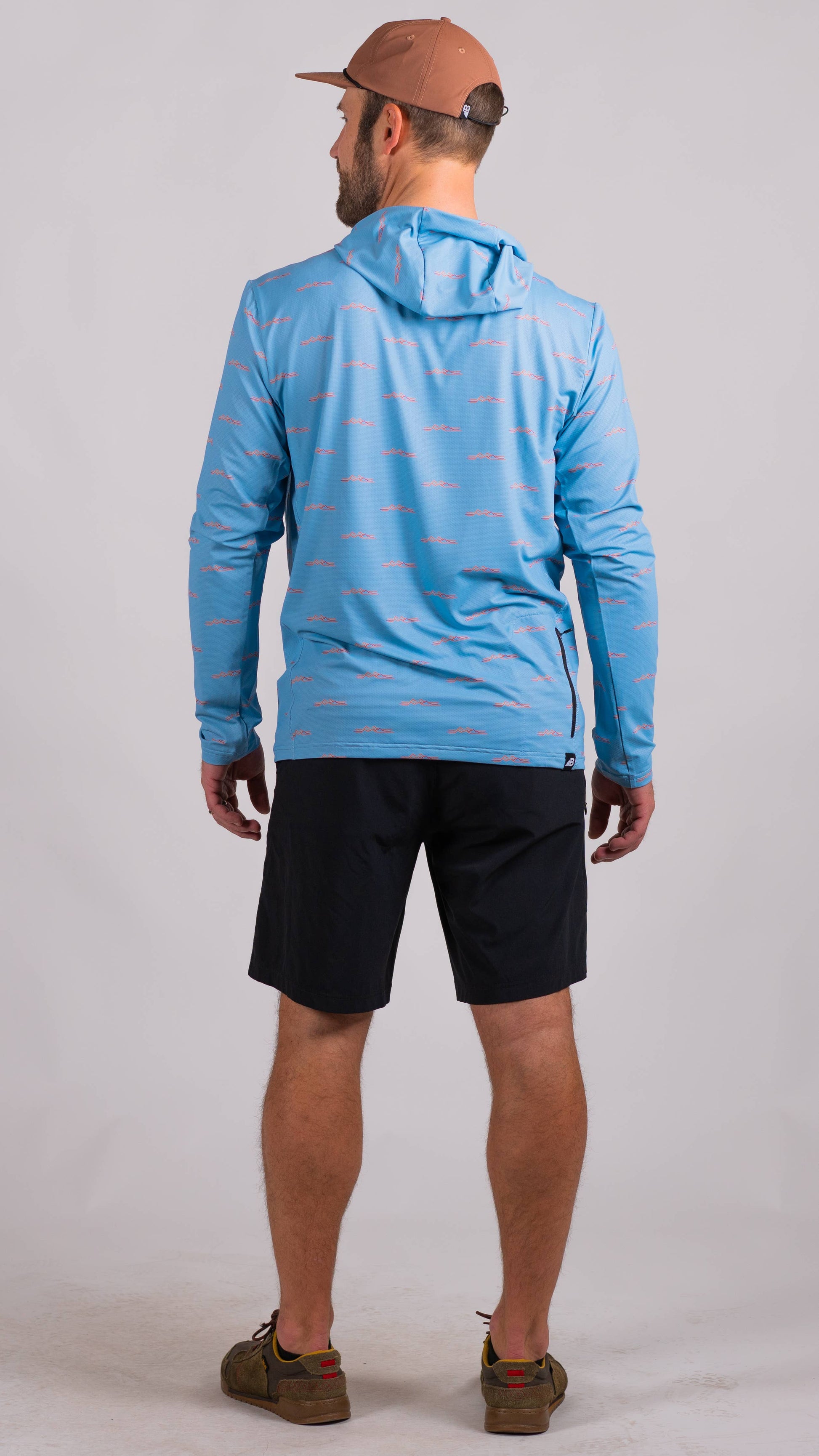 A man is wearing a Belong Designs Men's Sun Hoodie in Green Block, paired with black shorts. The hoodie features a small black logo on the left chest and offers UPF 50+ protection. He is standing against a plain, light-colored background, ready for outdoor activities. His head is not visible in the image.