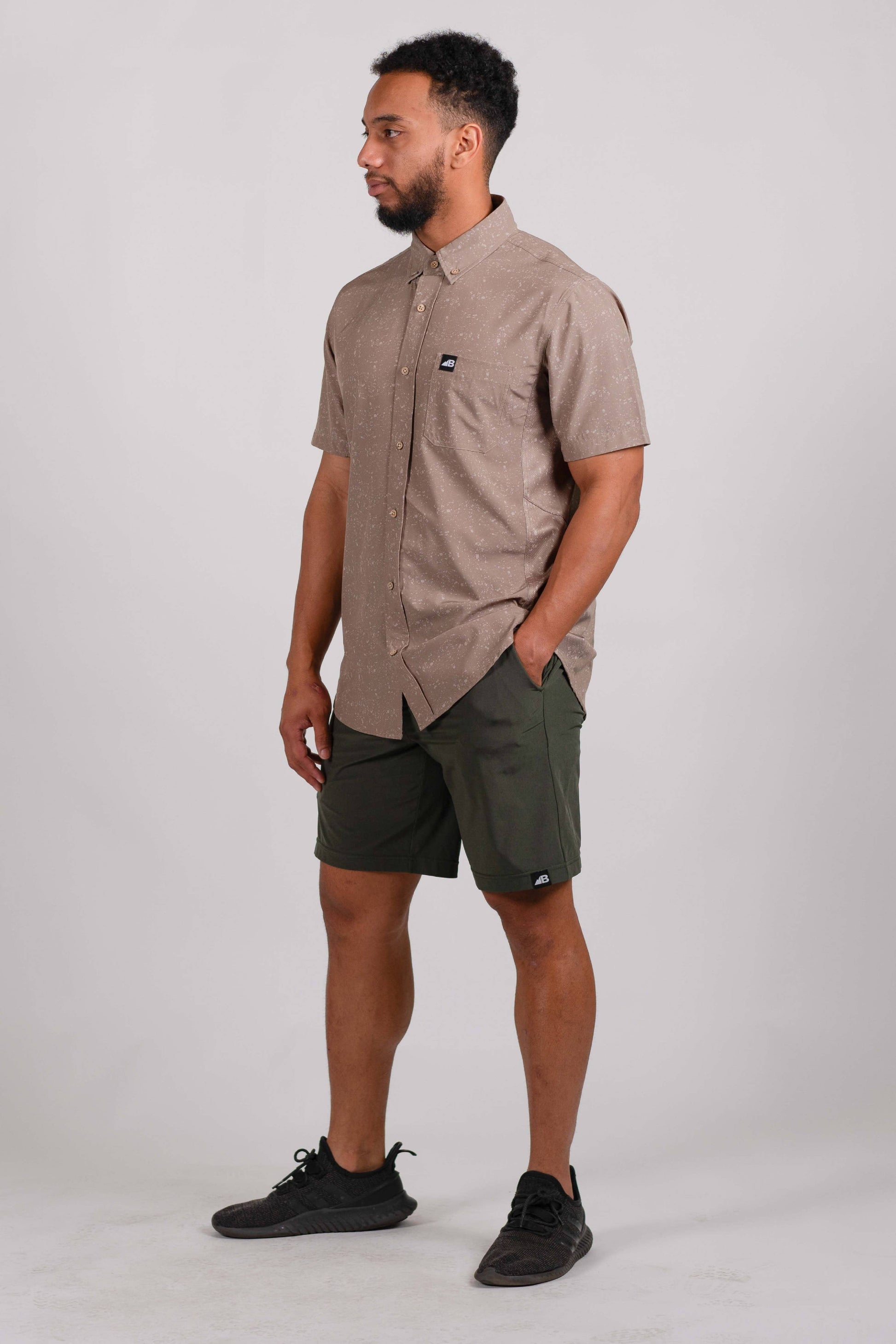 The Vista Stretch Button Down from Belong Designs features a modern, casual design in Summit Teal. This short-sleeve shirt includes a buttoned-down collar and is crafted from wrinkle-resistant fabric. It also comes with a small chest pocket adorned with a logo patch reading "Belong Designs.