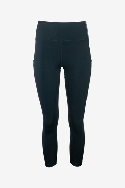 The Trailhead 7/8 Leggings from Belong Designs are black athletic leggings with a high waist and calf-length cut. They feature a colorful striped pattern in shades of purple and blue on the waist and leg panels. Crafted from PrimaFlex material, these multi-pocketed leggings also display a small logo on the left leg against a white background.