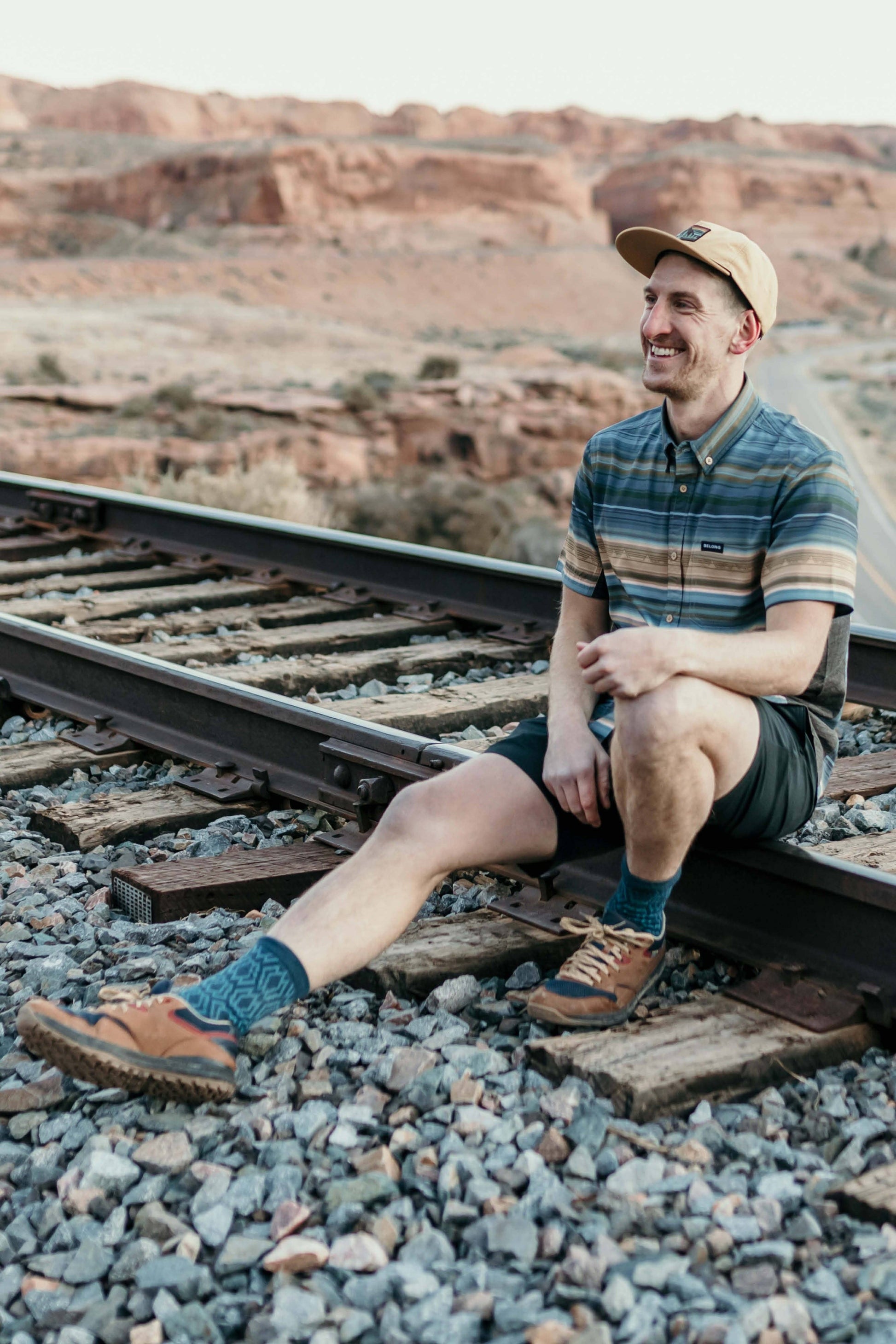 The Vista Stretch Button Down from Belong Designs features a modern, casual design in Summit Teal. This short-sleeve shirt includes a buttoned-down collar and is crafted from wrinkle-resistant fabric. It also comes with a small chest pocket adorned with a logo patch reading "Belong Designs.
