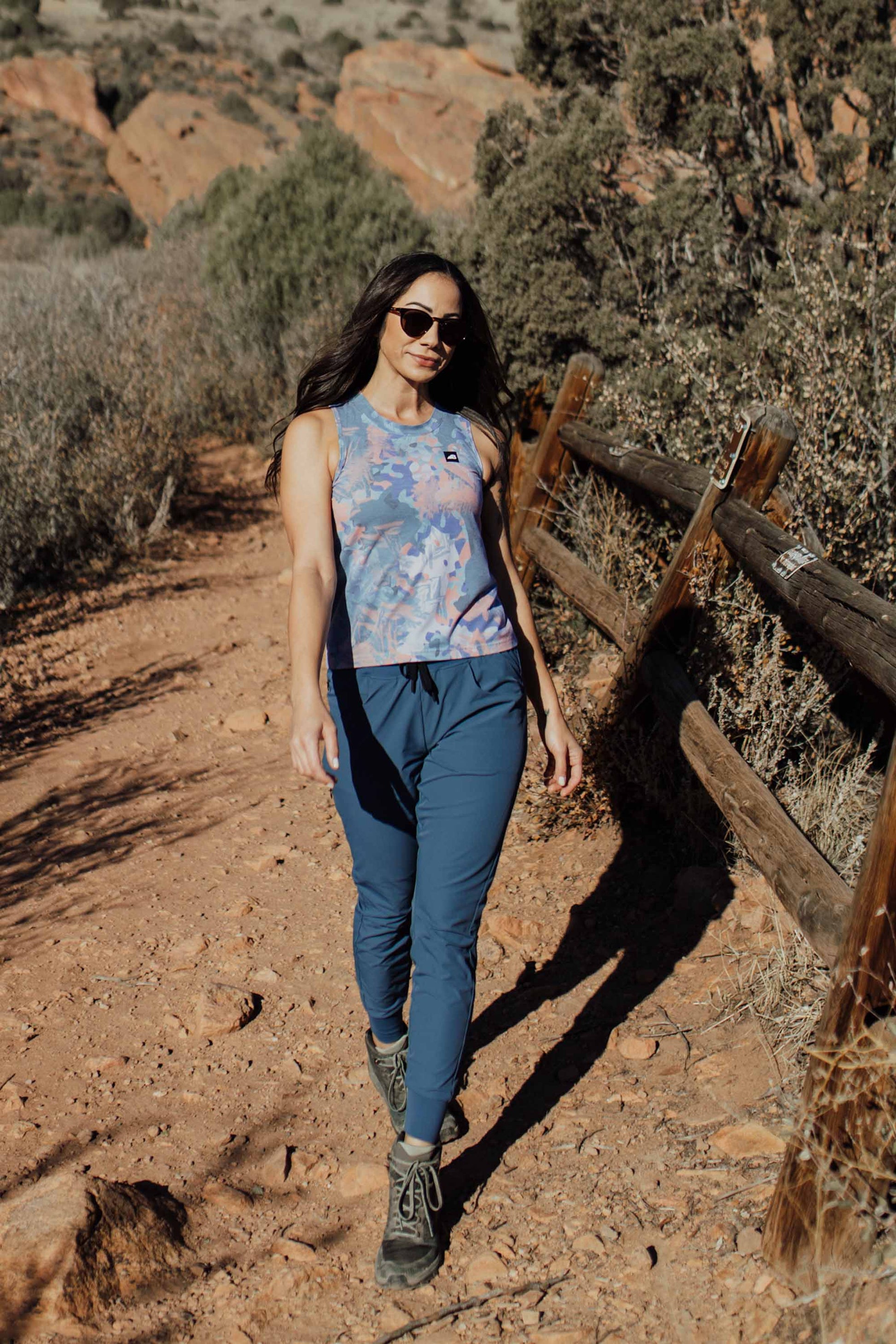 A person wearing Belong Designs' Rocky Mountain Joggers, crafted from durable and stretchy material, stands against a plain background. They are dressed in a dark green cropped top paired with matching athletic pants featuring a drawstring, complemented by brown hiking boots with teal laces. The image is cropped to show the midriff down.
