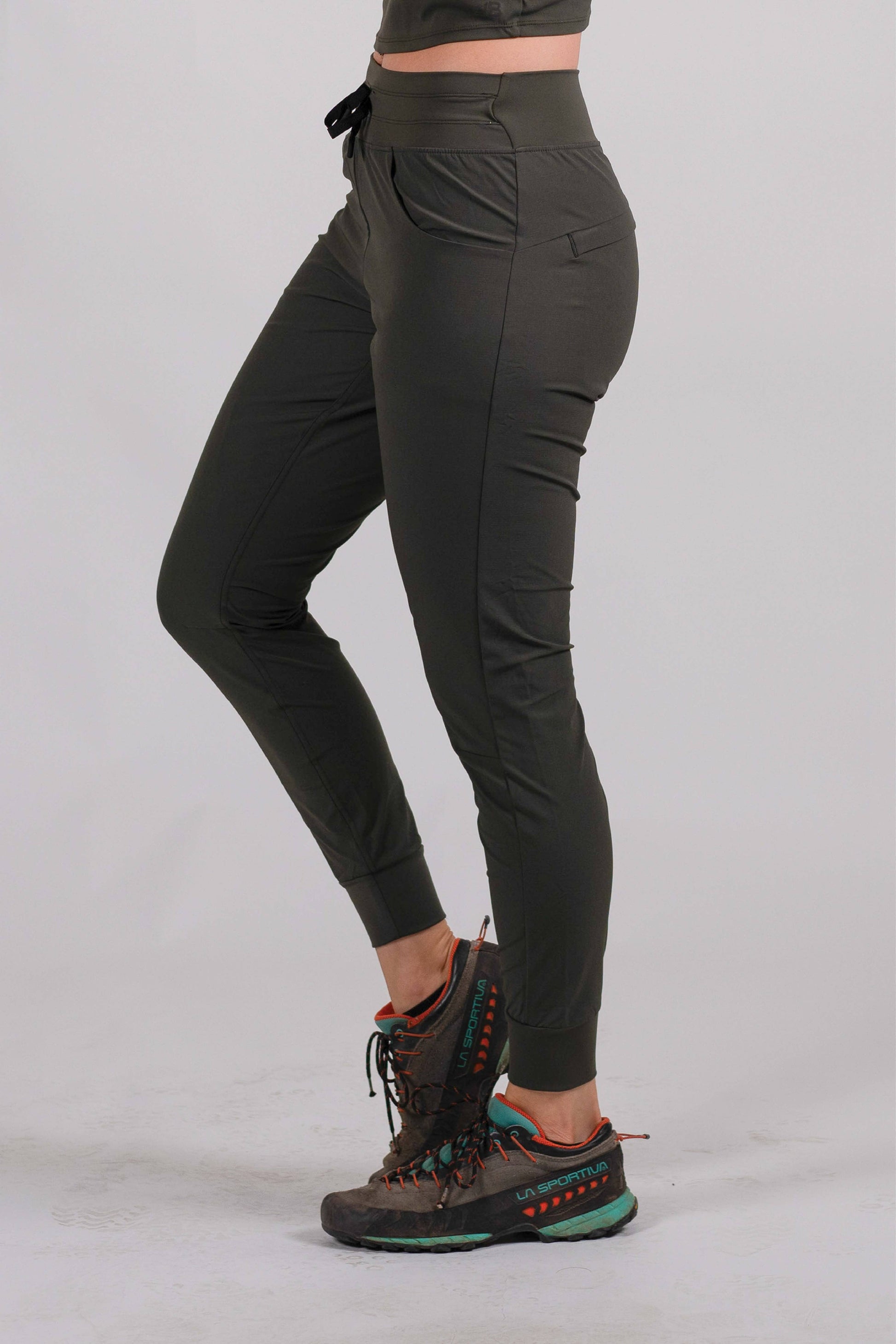 A person wearing Belong Designs' Rocky Mountain Joggers, crafted from durable and stretchy material, stands against a plain background. They are dressed in a dark green cropped top paired with matching athletic pants featuring a drawstring, complemented by brown hiking boots with teal laces. The image is cropped to show the midriff down.
