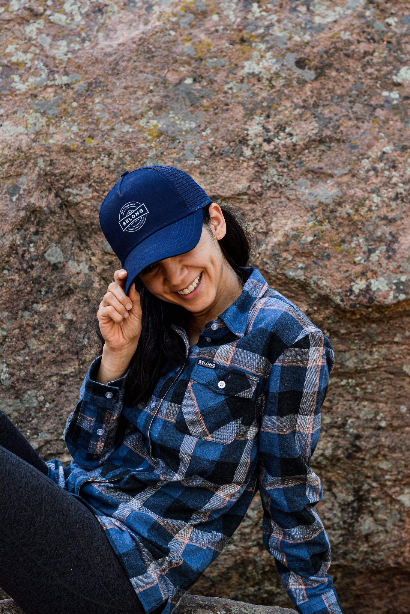 The Every Trail Trucker Hat by Belong Designs is a Black Mountain Brush trucker hat with a curved brim. The front panel showcases a vibrant wavy line design in shades of red, yellow, blue, and white with "BELONG" emblazoned prominently. The back and sides are made of breathable white mesh for added comfort.