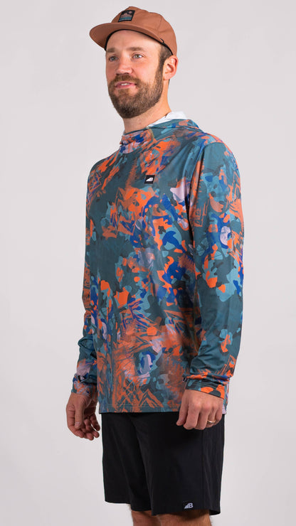 A man is wearing a Belong Designs Men's Sun Hoodie in Green Block, paired with black shorts. The hoodie features a small black logo on the left chest and offers UPF 50+ protection. He is standing against a plain, light-colored background, ready for outdoor activities. His head is not visible in the image.